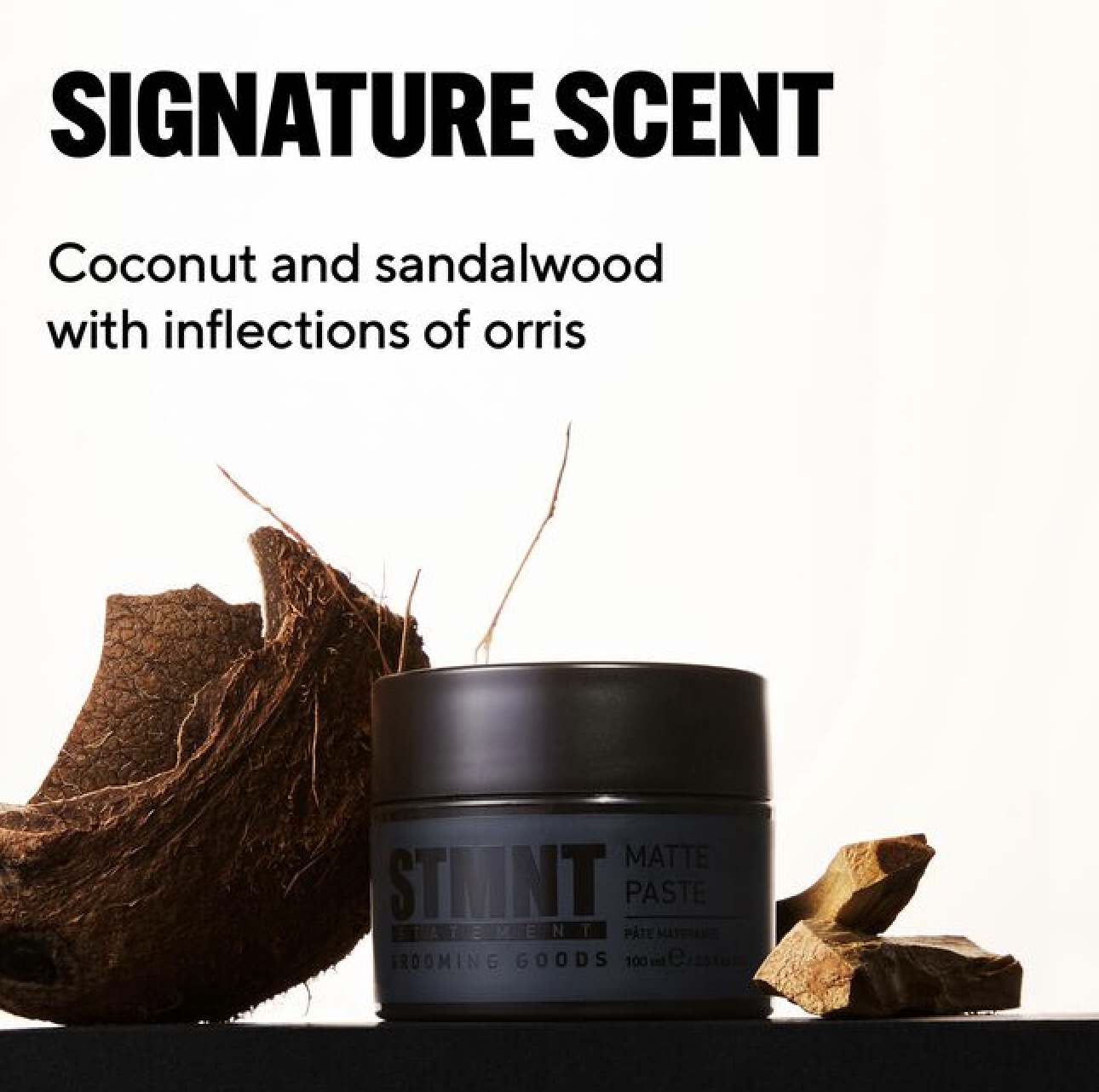 STMNT Grooming Goods Matte Paste jar beside coconut husk and sandalwood, signature scent coconut and sandalwood with inflections of orris